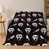 A dark flannel throw blanket featuring repeating white horror character faces and sharp blade motifs.