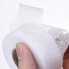 A hand is applying a roll of white iron-on fusible hem tape to a piece of fabric.