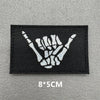 A black embroidered patch featuring a white hand gesture symbol on a gray background.