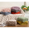 A stack of cozy checkered fleece throw blankets in various shades of pink, purple, gray, and orange resting on a light-colore