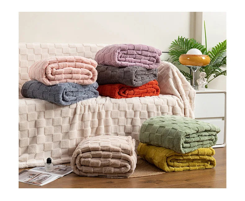 A stack of cozy checkered fleece throw blankets in various shades of pink, purple, gray, and orange resting on a light-colore
