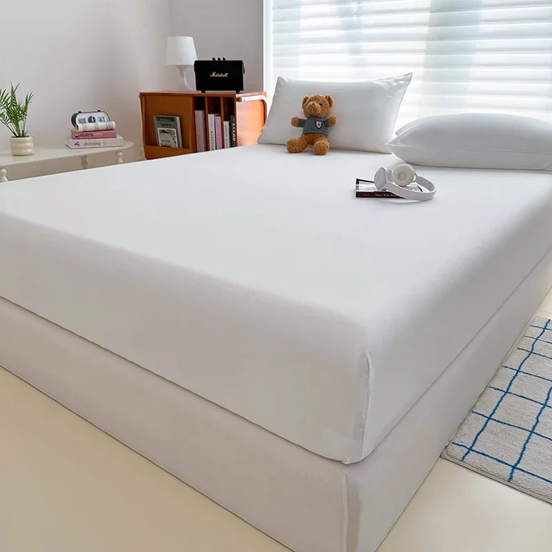 A white adjustable fitted bed sheet cover is displayed on a bed, next to books and a stuffed animal.
