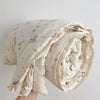 A rolled floral print muslin blanket in cream and green tones.