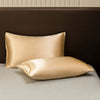 A pair of smooth satin pillows resting on a dark brown headboard and light gray bedding.