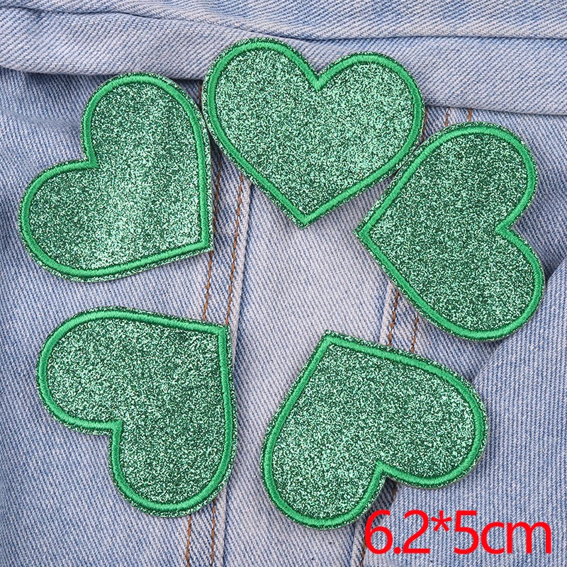 Five green glitter iron-on embroidered love heart star patches arranged on a gray denim fabric.