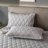 A stack of quilted, light gray pillow covers resting on a bed with a neutral headboard.