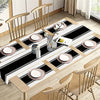 A set of minimalist black and white placemats and table flags laid out on a wooden table with dining chairs.