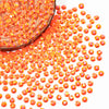 A close-up view of orange-red AB resin flatback rhinestones scattered on a white background.