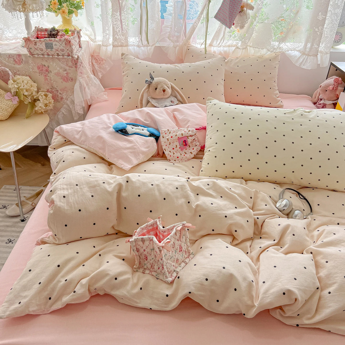 A pink polka dot duvet cover set with matching pillowcases and a small stuffed animal on a bed.