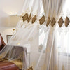 Sheer white and beige gauze curtains with gold embroidery framing a window.