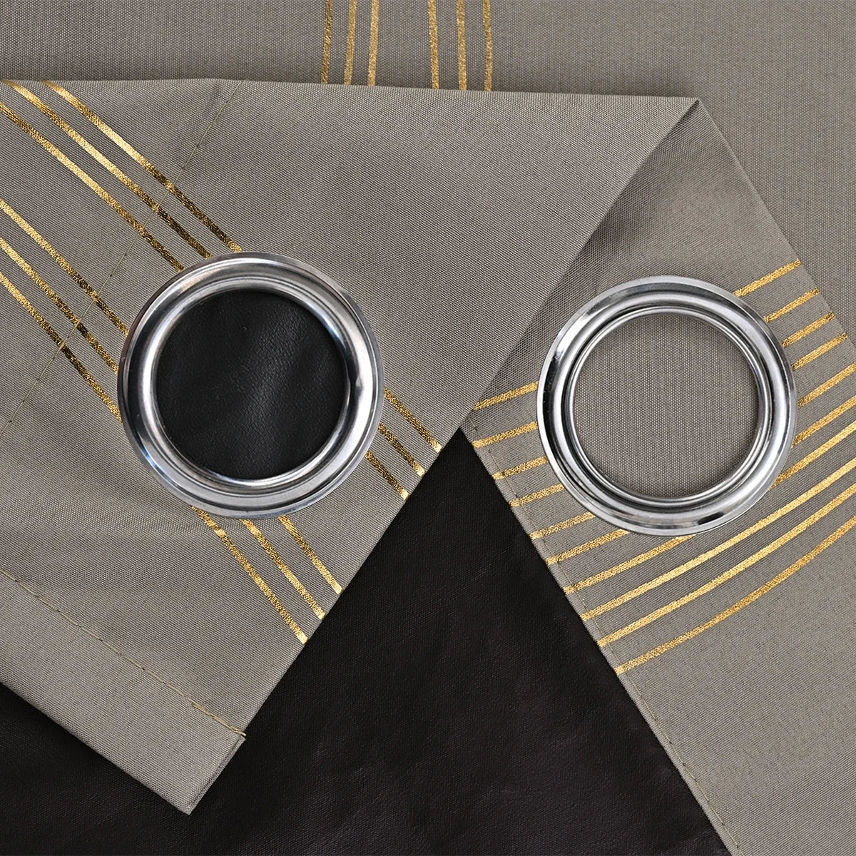 A silver grommet top curtain with a black fabric and gold striped fabric backing.