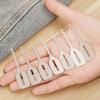 A hand holds a set of stainless steel needle threaders for hand sewing and embroidery on a wooden surface.