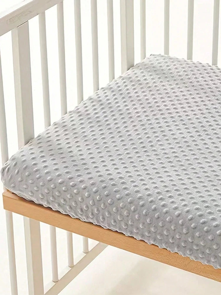 A soft gray plush mattress and diaper changing cover placed on a wooden crib rail.