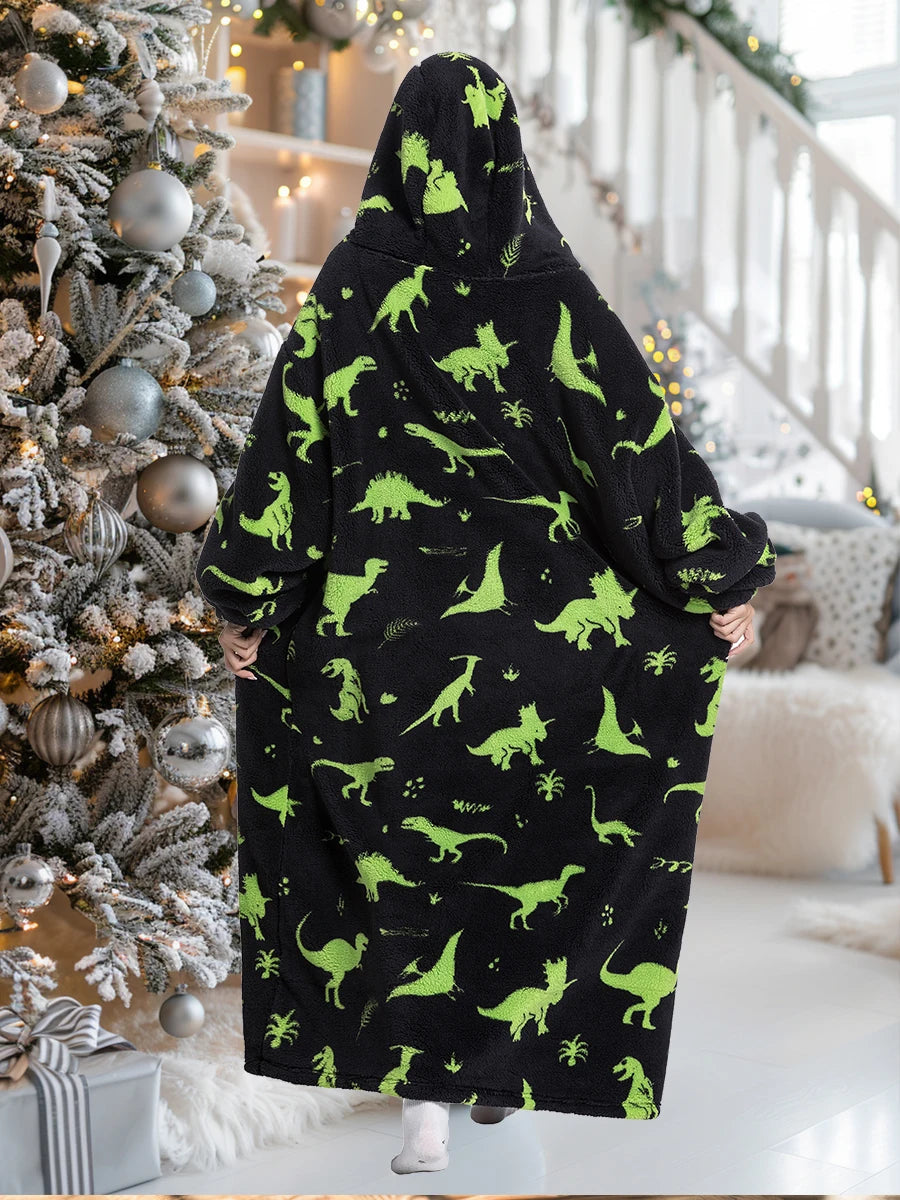 A person wearing a black and lime green patterned oversized sherpa fleece blanket hoodie standing in a bright indoor setting.