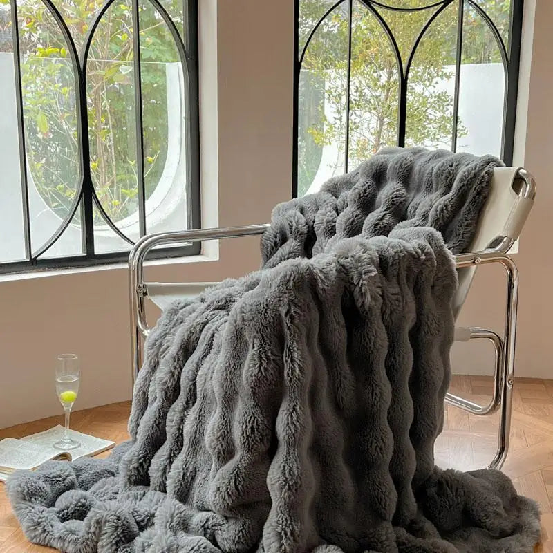 A gray plush faux fur throw blanket draped over a metal chair near a window.