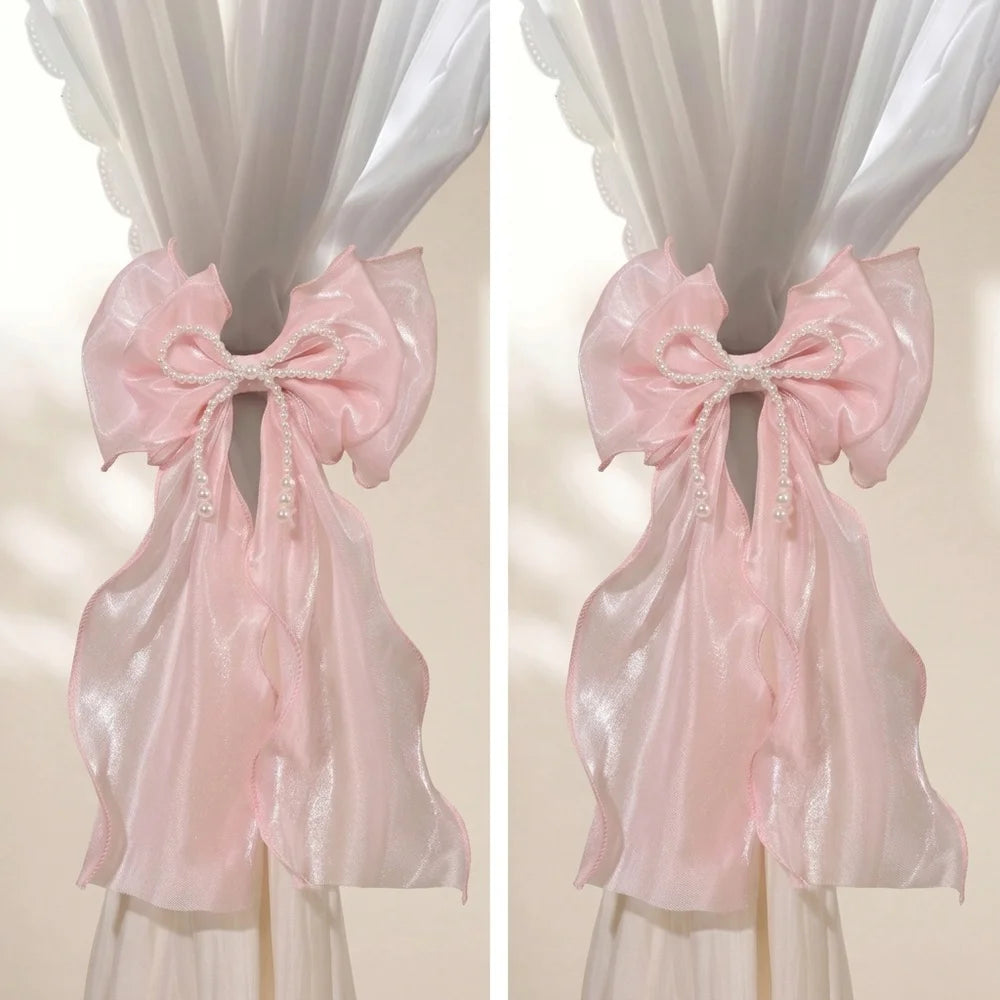 A pair of pink sheer ribbon bow curtain tiebacks displayed against a white background.