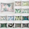 A collection of nine decorative pillows featuring various tropical leaf prints in shades of green, pink, and beige.