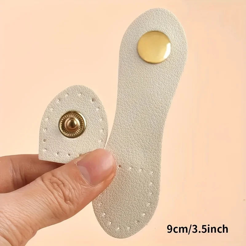 A set of eight light beige leather bag buttons, some with gold accents, being held by a hand.