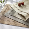 Three linen placemats with geometric embroidery and two small red fruits are displayed on a white surface.