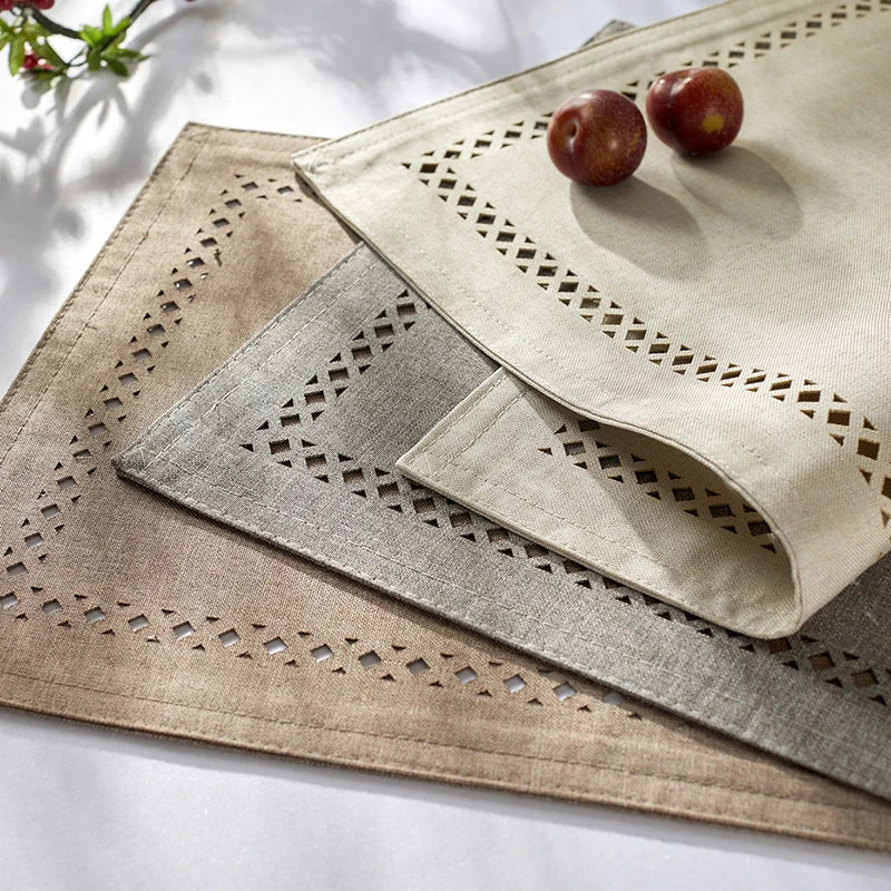 Three linen placemats with geometric embroidery and two small red fruits are displayed on a white surface.