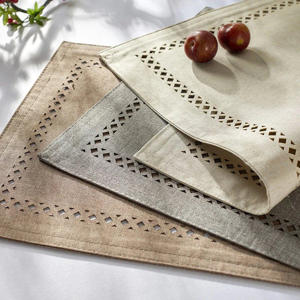 Three linen placemats with geometric embroidery and two small red fruits are displayed on a white surface.