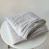 A stack of light gray pure French linen bed sheets folded neatly on a white round table.