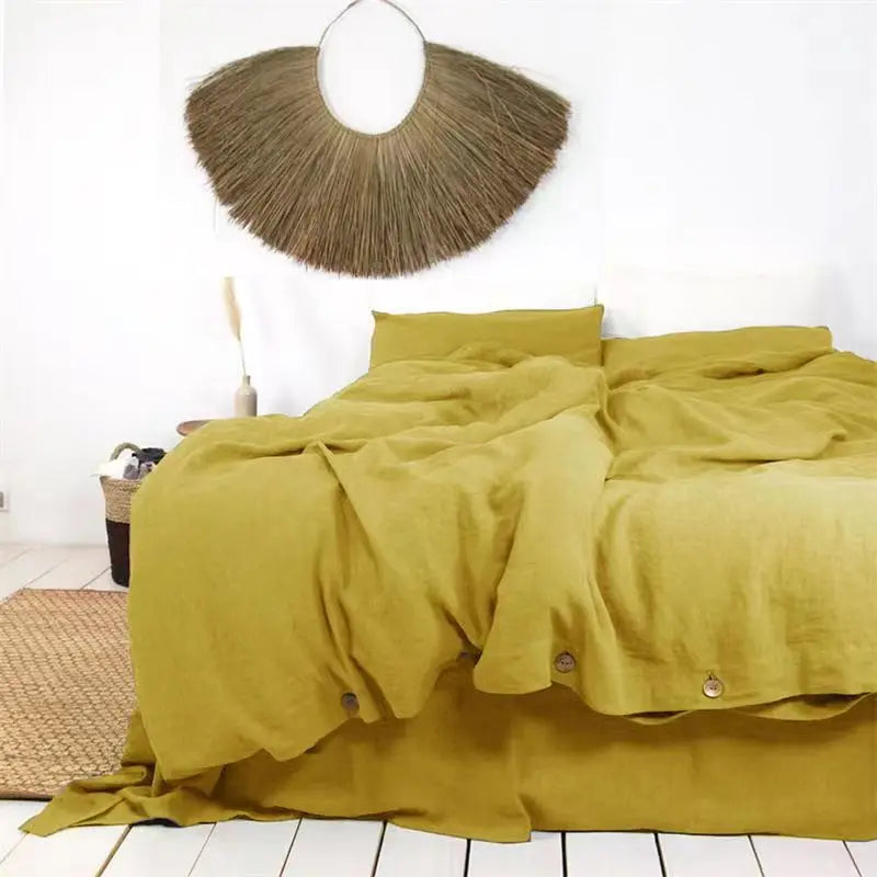 A luxurious olive green French linen duvet cover draped over a bed, with a natural fiber wall mirror above.