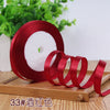 Roll of red satin ribbon with a white candle inside on a wooden surface