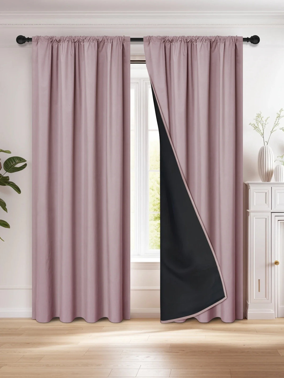 A pair of floor-length blackout curtains in mauve pink and black hanging in a window frame.