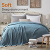 A soft blue linen throw blanket draped over a bed in a light-colored bedroom setting.