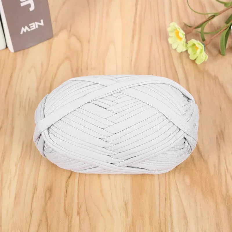A ball of light gray flat thread yarn for crafting and sewing placed on a wooden surface.