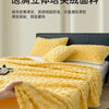 A bright yellow ultra-soft coral fleece blanket draped over a white bed, with a hand holding the fabric.