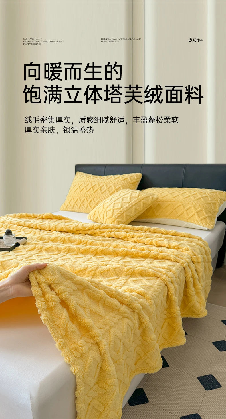 A bright yellow ultra-soft coral fleece blanket draped over a white bed, with a hand holding the fabric.