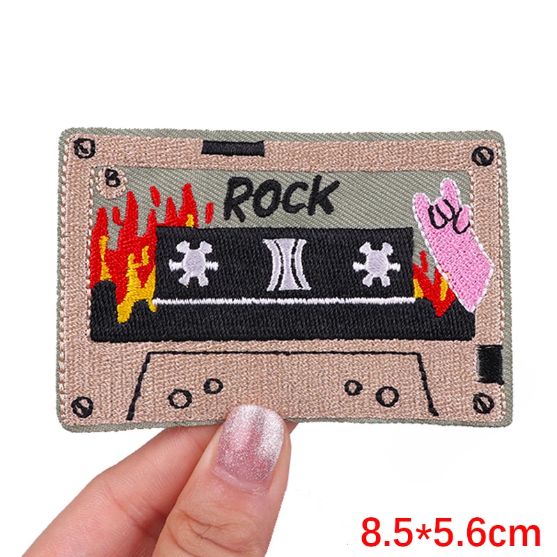 A rectangular embroidery patch featuring the word ROCK and a rose skull design on a beige fabric background.