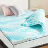 A bright blue and white marbled memory foam mattress topper is displayed on a bed with pink and gray pillows.