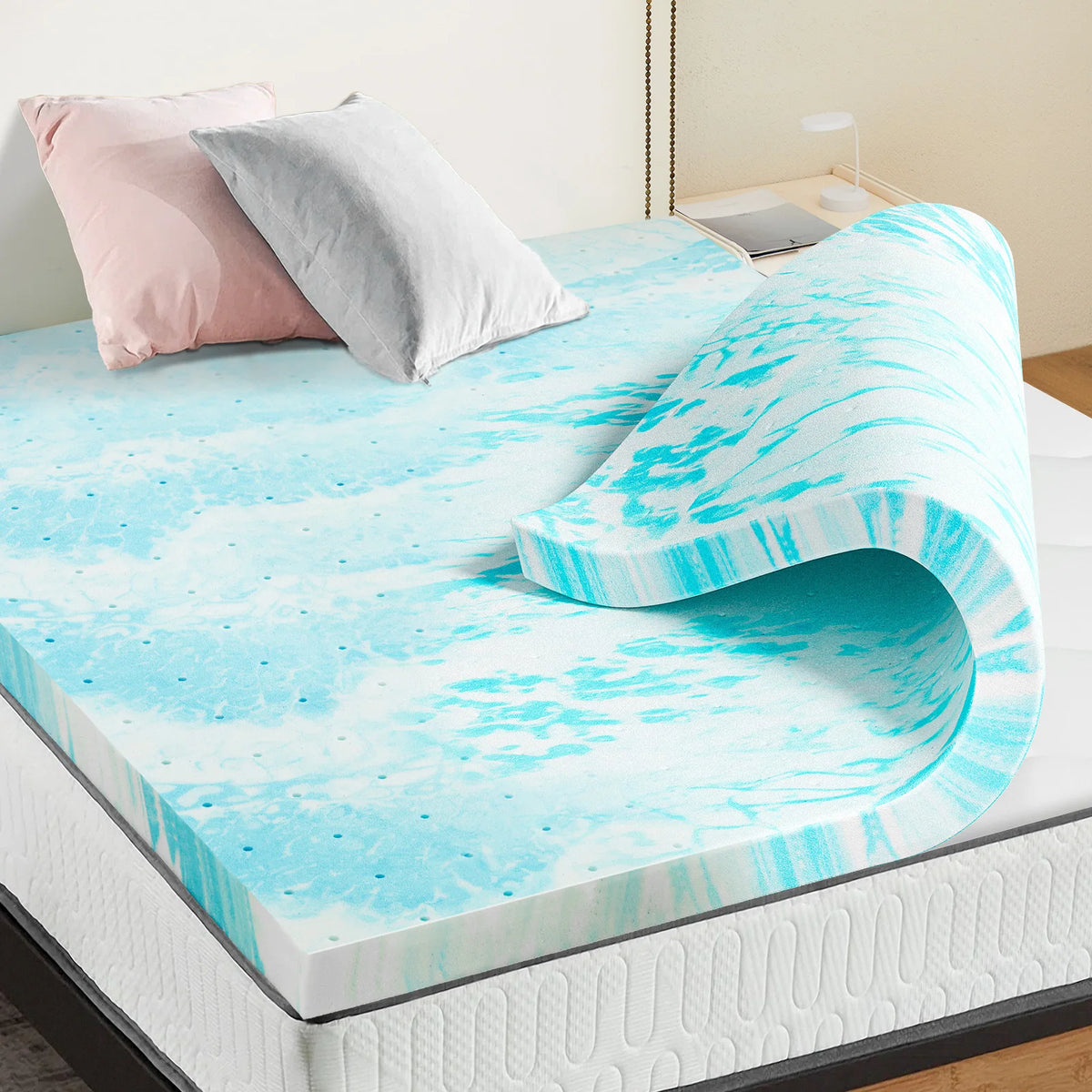 A bright blue and white marbled memory foam mattress topper is displayed on a bed with pink and gray pillows.