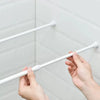Hands adjusting a white adjustable metal curtain rod against a white tiled wall.