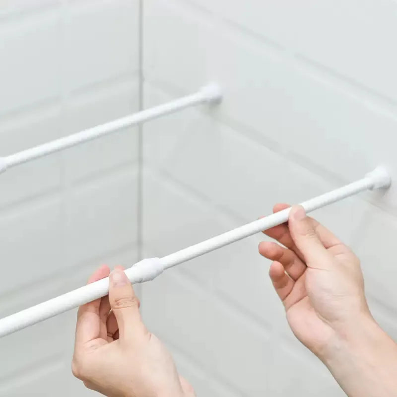 Hands adjusting a white adjustable metal curtain rod against a white tiled wall.
