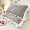Gray ruffled princess pillowcases with white trim displayed on a bed.
