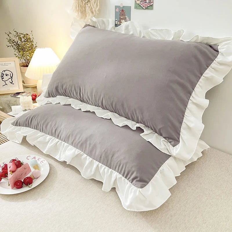 Gray ruffled princess pillowcases with white trim displayed on a bed.