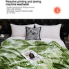 A green and white tie-dye flannel fleece throw blanket is displayed on a bed with a black patterned pillow.