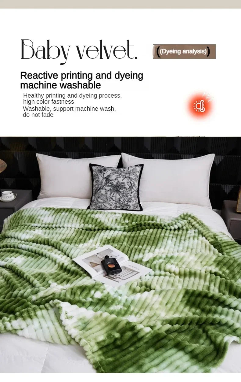A green and white tie-dye flannel fleece throw blanket is displayed on a bed with a black patterned pillow.