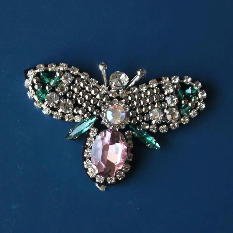 A handmade bee beaded sew-on patch featuring sparkling silver and pink stones set on a fabric background.