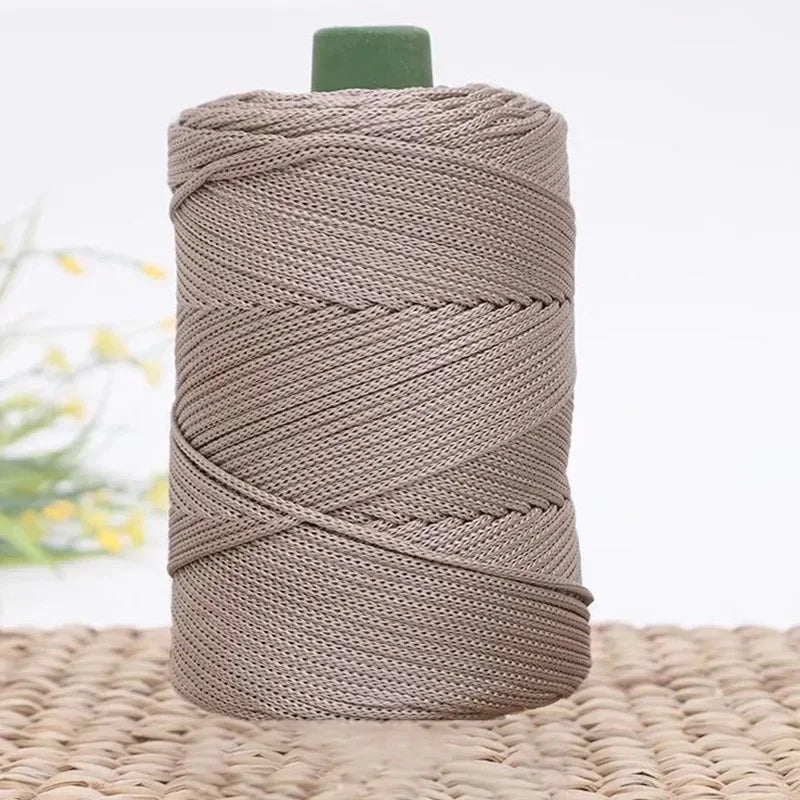 A spool of gray 3mm ice rope crochet yarn with a green cap resting on a woven mat.