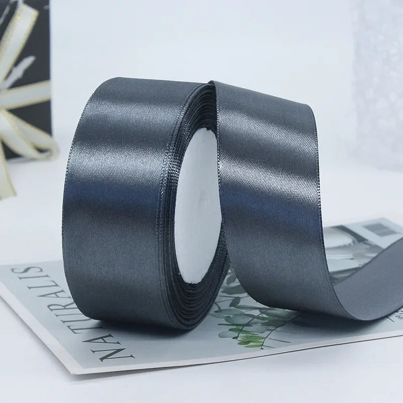 Roll of dark gray satin ribbon with a white center, lying on a sheet of paper.