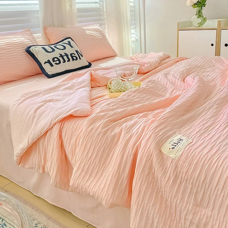 A pink Korean style seersucker summer quilt set displayed on a bed with white and pink pillows.