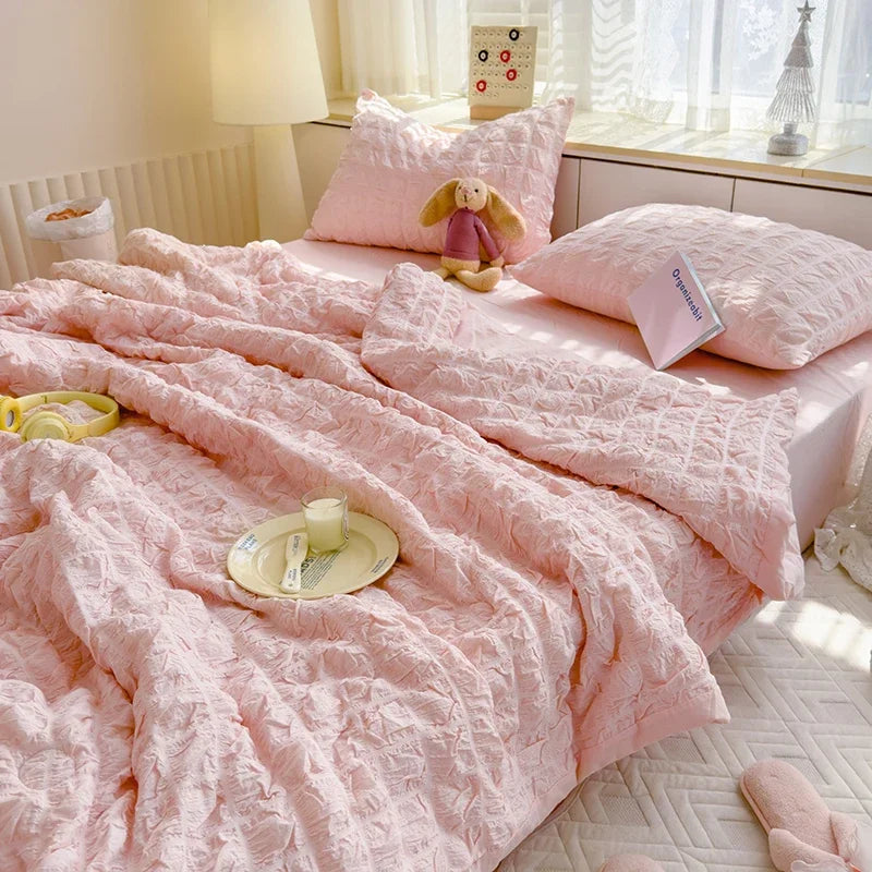 Pink summer seersucker quilt comforter spread on a bed with a stuffed animal and white bedding