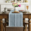 A blue embroidered cotton linen table runner with white tassels placed on a wooden table.