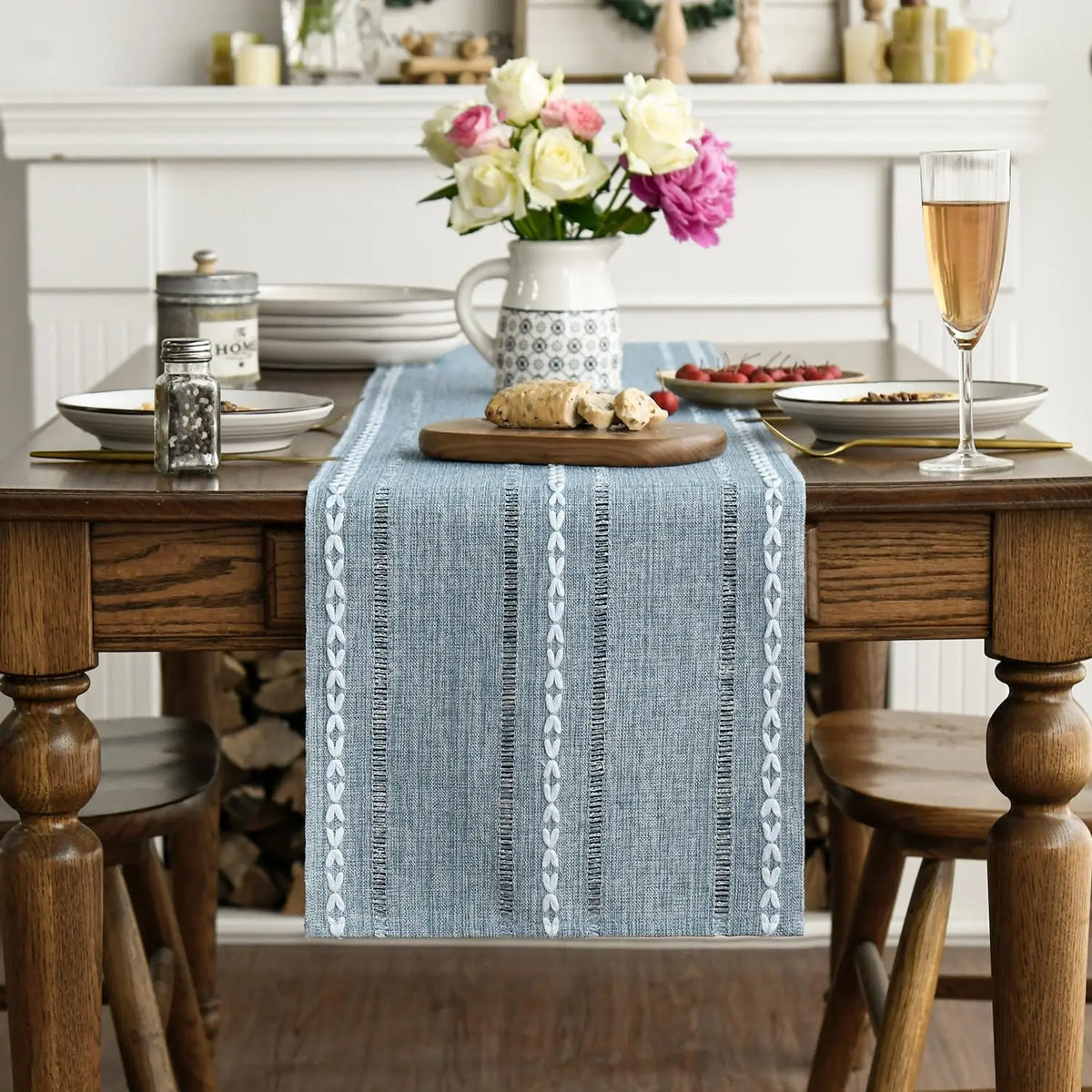 A blue embroidered cotton linen table runner with white tassels placed on a wooden table.