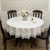 A round white embroidered lace tablecloth set for a meal with a vase of white roses and a teacup.